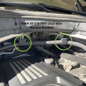 May include: An engine bay view featuring black wire harness brackets. The brackets are holding a black corrugated tube. The text "BMW X5 E70 2007-2013 Wire Harness Brackets" is visible.