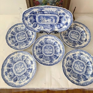 Może przedstawiać: Zestaw antycznych niebiesko-białych porcelanowych naczyń. Zestaw zawiera sześć talerzy i owalny półmisek. Każdy element przedstawia szczegółową scenę krajobrazu w centralnym ośmiokącie i ozdobnej obwódce.