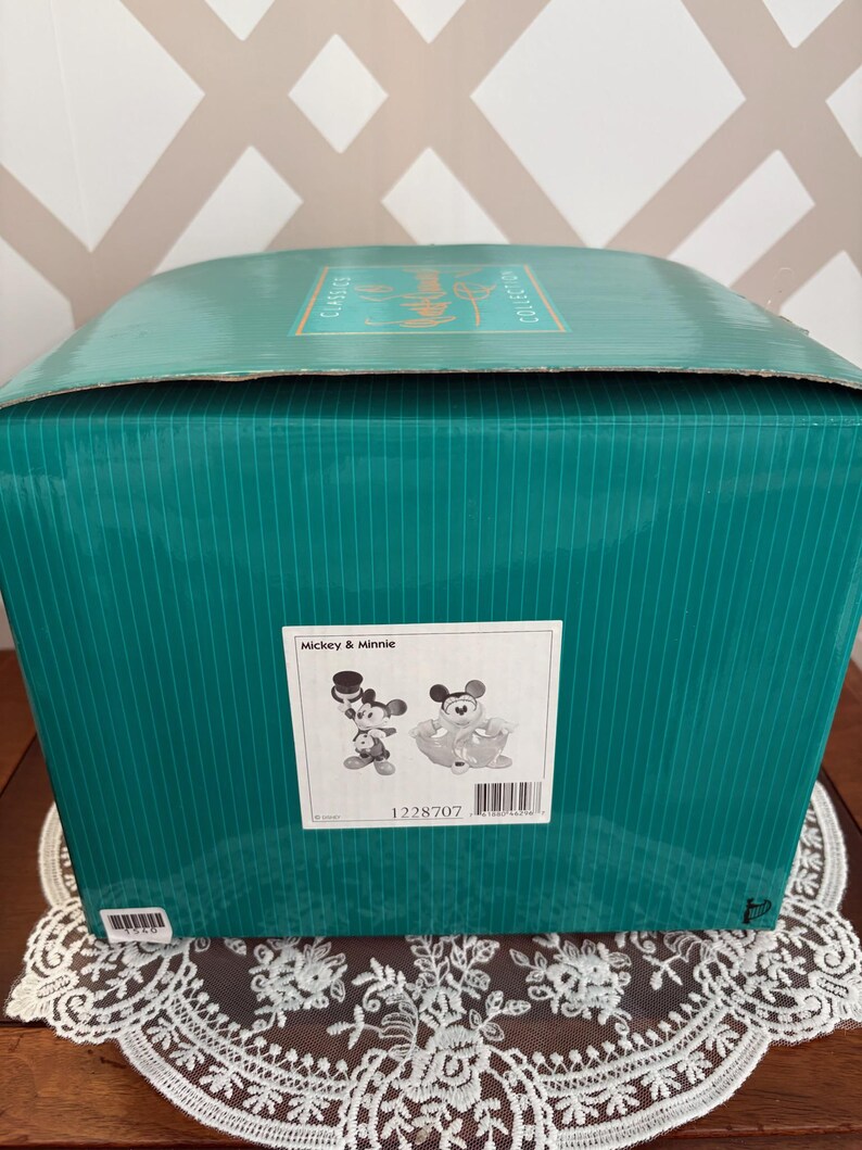 May include: A teal box with vertical lines, featuring a label with Mickey & Minnie illustrations. The box is on a table with a white lace doily. The top of the box has the words "Classics Collection".