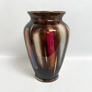 Może przedstawiać: Brązowy ceramiczny wazon z błyszczącym wykończeniem. Pionowe pociągnięcia pędzla w kolorze czerwonym, pomarańczowym, niebieskim i białym są zaakcentowane złotymi liniami. Wazon ma złoty brzeg u góry i u dołu i ma około 25 cm wysokości.