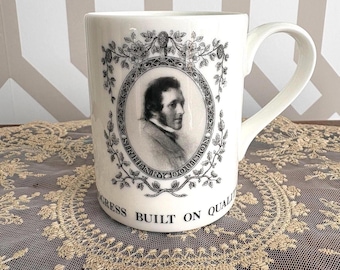 May include: A white ceramic mug featuring a black and white portrait of Sir Henry Doulton inside an oval frame surrounded by floral motifs. The text "PROGRESS BUILT ON QUALITY" is printed in black capital letters along the base of the mug.