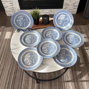 Puede incluir: Un conjunto de platos de cerámica azules y blancos con un patrón Willow clásico. Los platos están dispuestos sobre una mesa redonda, mostrando sus intrincados diseños y su estética tradicional. Los platos son de varios tamaños y formas.