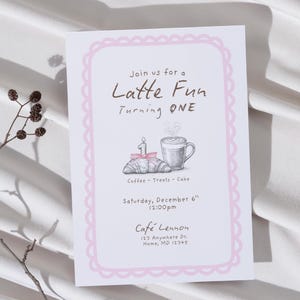 Op de afbeelding: Een witte uitnodigingskaart met een roze geschulpte rand. De tekst "Join us for a Latte Fun Turning ONE" wordt weergegeven. Illustraties van een croissant, koffiekopje en kaars zijn inbegrepen. De kaart bevat ook de datum, tijd en locatie.