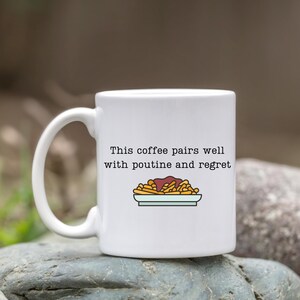 May include: White ceramic coffee mug with a black outline of a plate of poutine and the text "This coffee pairs well with poutine and regret."
