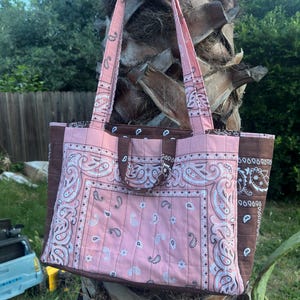 Puede incluir: Un bolso tote acolchado con un estampado de cachemira tipo bandana en rosa y blanco en los paneles frontal y posterior, contrastado por paneles laterales y asas de color marr&oacute;n oscuro. Incluye dos correas largas y dos asas cortas.