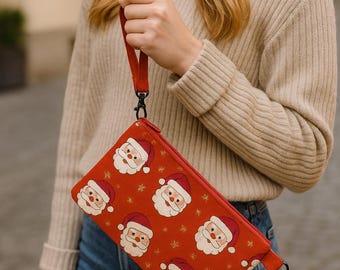 Op de afbeelding: Een rode rechthoekige clutch met een polsbandje, met een herhaald patroon van Sinterklaasgezichten en sneeuwvlokken. De clutch heeft een ritssluiting en zwarte metalen hardware. De achtergrond is wazig.