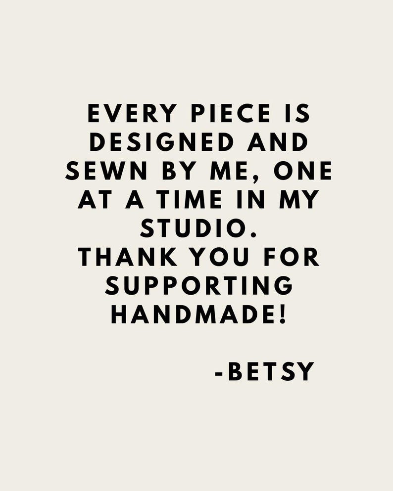 May include: A rectangular sign with a light beige background and black text that reads: EVERY PIECE IS DESIGNED AND SEWN BY ME, ONE AT A TIME IN MY STUDIO. THANK YOU FOR SUPPORTING HANDMADE! -BETSY. The text is centred and in a sans-serif font.