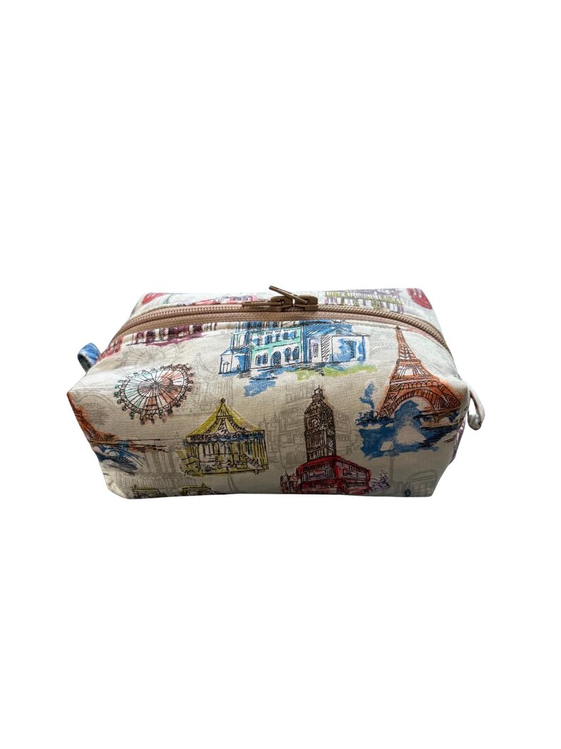 A rectangular fabric cosmetics pouch featuring a colorful sketch print of famous landmarks and a brown zippered closure across the top.