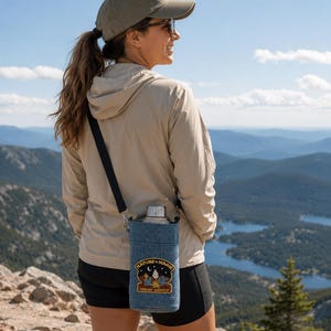 May include: A blue denim water bottle holder with a black adjustable shoulder strap. The holder features a rectangular embroidered patch with the text "NATURE IS MAGIC" and "TREAD LIGHTLY" above and below a desert landscape graphic.