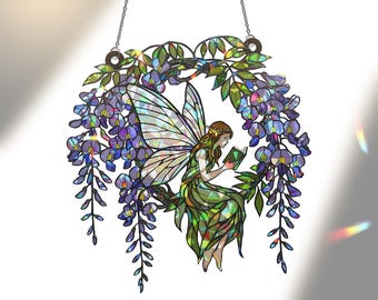 Peut inclure: Un attrape-soleil en vitrail représentant une fée aux ailes irisées assise au milieu d'une couronne de fleurs de glycine violettes et de feuilles vertes. La fée lit un petit livre vert, l'ensemble étant suspendu par une chaîne en métal.