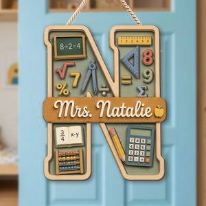 May include: A wooden letter N wall sign featuring a light green background with various school-themed math icons including a chalkboard with 8÷2=4, a ruler, a compass, a calculator, an abacus, and a pencil. The center bar displays the text Mrs. Natalie.