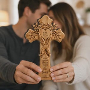 May include: A light brown wooden cross featuring a carved heart at the centre with the text EST. 2024, the names Jacob and Christina, and the phrase I HAVE FOUND THE ONE WHOM MY SOUL LOVES, followed by SONG OF SOLOMON 3:4, with tree branch details.