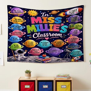 Może przedstawiać: Prostokątny gobelin ścienny z ciemnoniebieskim tłem kosmosu, planetami, gwiazdami i rakietą. Tekst brzmi In MISS MILLIE'S Classroom, otoczony motywacyjnymi hasłami na kolorowych planetach, astronautą i stosem książek.
