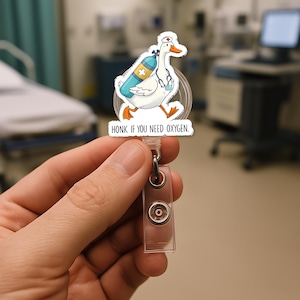 Könnte beinhalten: Eine weiße Gans mit einer Krankenschwestermütze und einem Sauerstofftank. Die Gans befindet sich auf einem durchsichtigen, einziehbaren Ausweishalter mit dem Text "HONK IF YOU NEED OXYGEN."