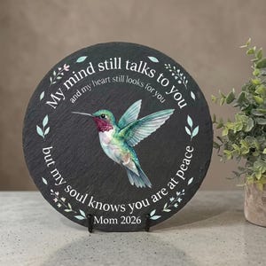 May include: A round black slate plaque featuring a watercolor hummingbird in the center. The text reads: My mind still talks to you and my heart still looks for you but my soul knows you are at peace. The bottom includes the text Mom 2026.