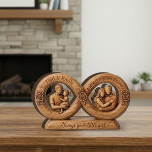 May include: Wooden infinity sign sculpture with carved figures of a family and the text "Dad & Emily" and "A love that grows forever." The base reads "Always your little girl." The sculpture is brown and sits on a wooden surface.