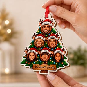 May include: A Christmas tree-shaped wooden ornament featuring six circular photo cutouts of people wearing Santa hats. Each face is labeled with a name: James, Emma, Michael, Olivia, Noah, and Sophia. The base reads The Smith Family.
