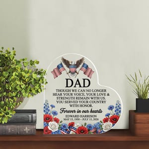 Puede incluir: Placa conmemorativa en forma de corazón con la palabra "DAD" y el texto "Forever in our hearts". Presenta un águila, banderas americanas y detalles florales en rojo, blanco y azul. Incluye el nombre Edward Harrison y las fechas 15 de mayo de 1950 - 15 de julio de 2026.