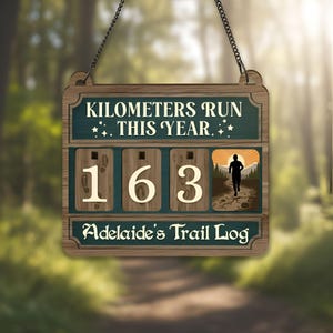 May include: Wooden sign with the text "Kilometers Run This Year" and "Adelaide's Trail Log." The sign displays the number "163" and a silhouette of a runner. The sign is hanging from a chain.