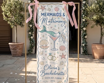 May include: A vertical rectangular banner with pink ribbons at the top, featuring the text "MERMAIDS & Matrimony", "Olivia's Bachelorette", "SIESTA KEY, FLORIDA", and "2026". The design includes a mermaid in a martini glass, shells, and rings.