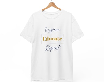 May include: White t-shirt with the words "Inspire Educate Repeat" in navy blue and gold lettering. The words are arranged vertically, with "Educate" inside a gold-coloured rectangle. The t-shirt is hanging on a wooden hanger.