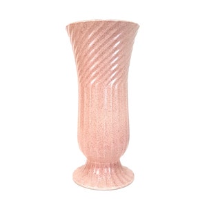 May include: A tall, pink ceramic vase with a speckled finish. The vase has a flared top and a pedestal base. The body of the vase features a spiral design. The vase is a decorative item.