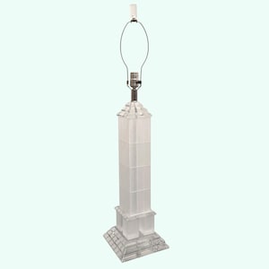 May include: A clear, rectangular table lamp with a geometric design. The lamp features a square base, a tall, column-like body, and a metal lamp holder. The lamp is topped with a light bulb and a wire frame for a lampshade.