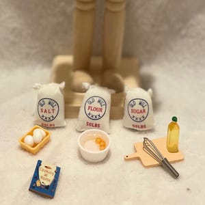 Könnte beinhalten: Eine Holz-Nussknacker-Figur mit Trommel und Trommelstöcken, begleitet von Miniaturbeuteln mit Salz, Mehl und Zucker sowie anderem Küchenzubehör. Die Beutel sind mit "50LBS" beschriftet.