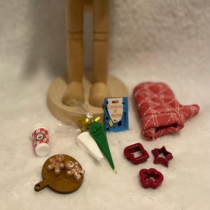 Könnte beinhalten: Eine Holz-Nussknacker-Figur mit hohem Hut, stehend auf einem Holzsockel. Zubehör: roter Ofenhandschuh, Ausstecher, kleines Kochbuch und Spritzbeutel. Ein kleines Holzbrett mit Lebkuchenmännern.