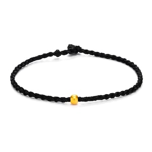 May include: A black braided cord bracelet with a single gold-colored bead in the center. The bracelet is knotted at the ends, and the design is simple and elegant.
