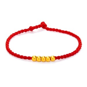May include: A red braided bracelet with five gold beads. The bracelet is knotted at the ends and is displayed against a white background. The gold beads are evenly spaced along the bracelet.