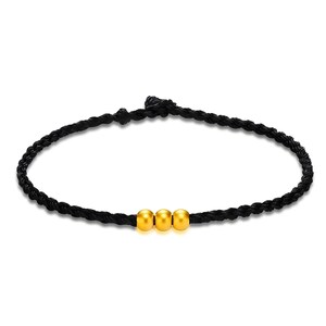 May include: A black braided bracelet featuring three gold-colored beads. The bracelet is made of a dark, woven material and has a simple, elegant design. The beads are evenly spaced and add a touch of shine.