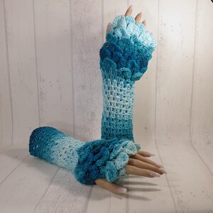 May include: A pair of blue and white crocheted fingerless gloves with a scale pattern on the back of the hand.