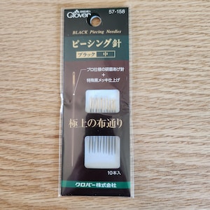 May include: A package of 10 black piecing needles for quilting. The needles are made by Clover and are designed for use with fine fabrics. The package is labeled "Black Piecing Needles" and "極上の布通り" which translates to "Excellent Fabric Flow".