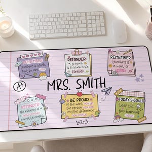 以下が含まれることがあります： 中央に「MRS. SMITH」という文字が書かれた、薄紫色の罫線入り紙風の長方形デスクマット。教師向けの感動的な引用が書かれた6枚のカラフルな付箋風グラフィック、A+の評価アイコン、紙飛行機や数式などの小さな落書きが描かれています。
