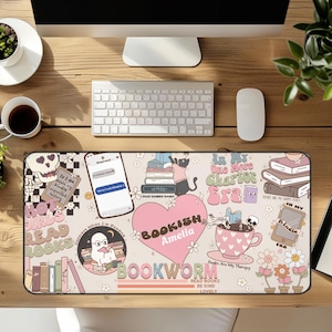 Könnte beinhalten: Eine beige Schreibtischunterlage mit einem farbenfrohen Design zum Thema Bücher. Die Unterlage zeigt Illustrationen von Büchern, einer Katze, einem Totenkopf, einer Teetasse und den Wörtern "BOOKWORM" und "READ BOOKS". Ein Telefon mit einer Textnachricht ist ebenfalls abgebildet.