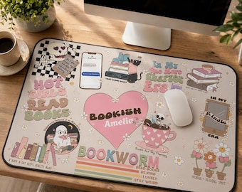 May include: A rectangular desk mat with a beige background featuring various illustrations including a pink heart with the text Bookish Amelia, a skull, a cat, stacks of books, a coffee cup, flowers, and text such as Hot Girls Read Books.