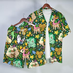 May include: A dark green shorts and short-sleeved shirt set with a vibrant pattern of cartoon characters, flowers, and lightning bolts. The shirt is open, revealing a white t-shirt. The set is designed for casual wear.