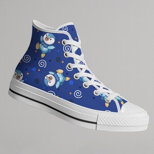 May include: High-top canvas sneaker in a vibrant blue, featuring a repeating pattern of cartoon penguins in flight. The design includes white swirls and dots. The shoe has a white rubber sole and toe cap, with white laces.