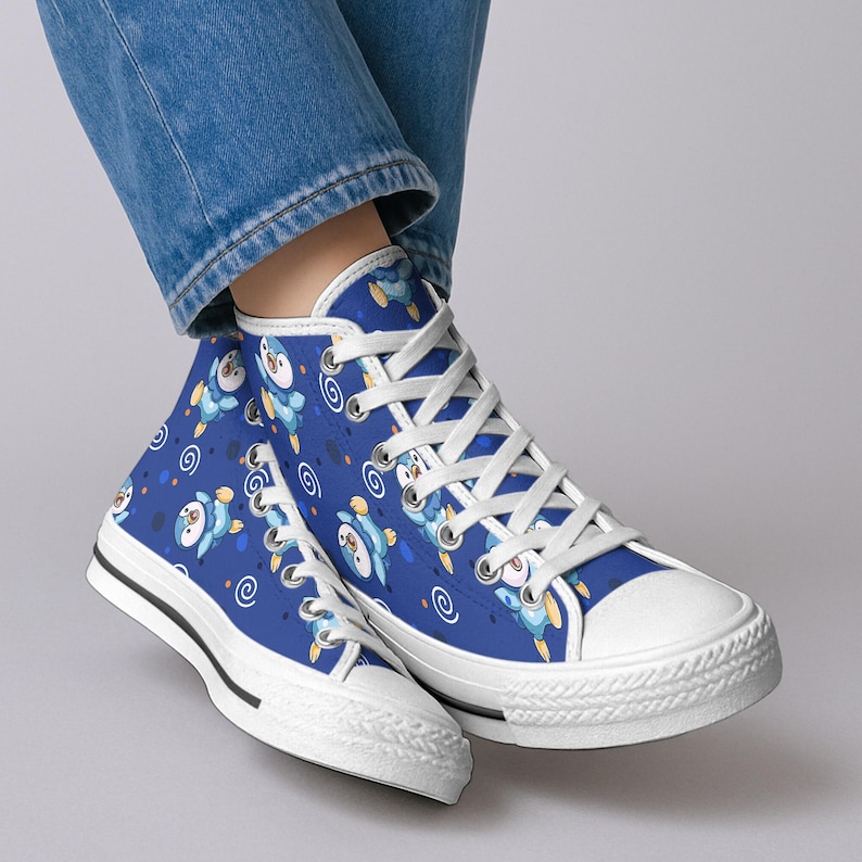 May include: Blue high-top sneakers with a white rubber sole and white laces. The sneakers feature a repeating pattern of cartoon penguins in blue and yellow. The shoes have a white toe cap and a black stripe along the sole.