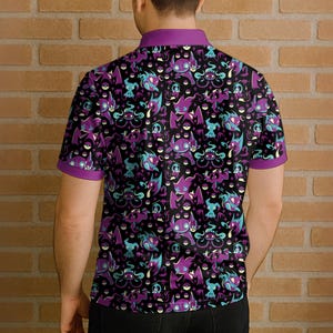 May include: Black polo shirt with a repeating pattern of purple, teal, and white cartoon characters. The shirt has a purple collar and sleeve trim. The design features various creatures on a black background.