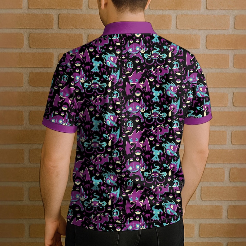 May include: Black polo shirt with a repeating pattern of purple, teal, and white cartoon characters. The shirt has a purple collar and sleeve trim. The design features various creatures on a black background.