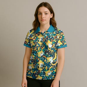 May include: A short-sleeved polo shirt with a vibrant pattern of yellow cartoon characters, flowers, and foliage on a navy blue background. The shirt has a teal collar and sleeve trim. The model is wearing black pants.