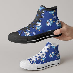 May include: Blue high-top sneakers with a penguin pattern. The sneakers have a black sole and laces, with a white midsole. The penguin design features a cartoon penguin in shades of blue and white, with spiral accents.