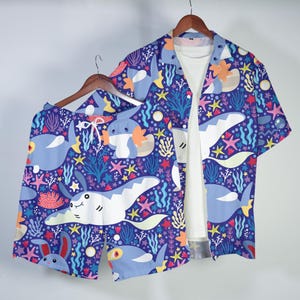 May include: A short-sleeve button-down shirt and matching shorts set featuring a dark blue background with a repeating pattern of white stingrays, blue aquatic creatures, orange coral, and colorful starfish. The shirt is worn over a white t-shirt.