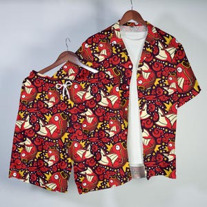 May include: A matching red and yellow patterned short-sleeve shirt and shorts set. The pattern features a repeating design of a red creature with yellow accents on a dark purple background. The shirt is open, revealing a white t-shirt underneath.