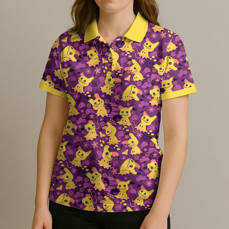 May include: Purple polo shirt featuring a repeating pattern of yellow cartoon characters, flowers, and clouds. The shirt has a yellow collar and sleeve trim. The design is a playful and colourful style.