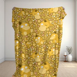 May include: A mustard-colored blanket featuring a repeating pattern of yellow cartoon characters, flowers, and fruit slices. The blanket is held up against a white wall, showcasing the design's details. The design includes a variety of floral and fruit elements.