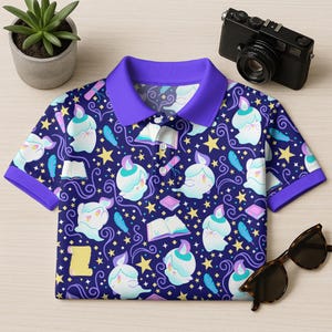 May include: A short-sleeved polo shirt with a dark blue background and a repeating pattern of cartoon ghosts, stars, books, and feathers. The shirt has a purple collar and sleeve cuffs. A pair of sunglasses and a camera are next to the shirt.