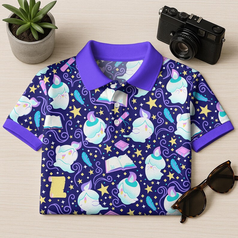 May include: A short-sleeved polo shirt with a dark blue background and a repeating pattern of cartoon ghosts, stars, books, and feathers. The shirt has a purple collar and sleeve cuffs. A pair of sunglasses and a camera are next to the shirt.